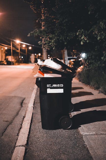 A person is seen depositing a brown paper bag filled with rubbish into a white waste bin with a black interior, likely for professional waste collection or disposal. The individual’s arm is visible,